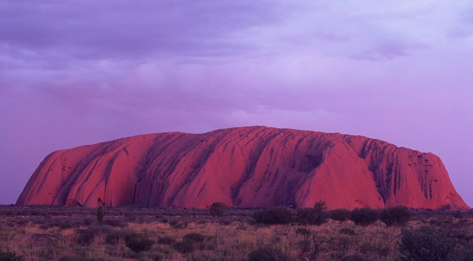 Uluru glowing deep red under a violet dusk sky