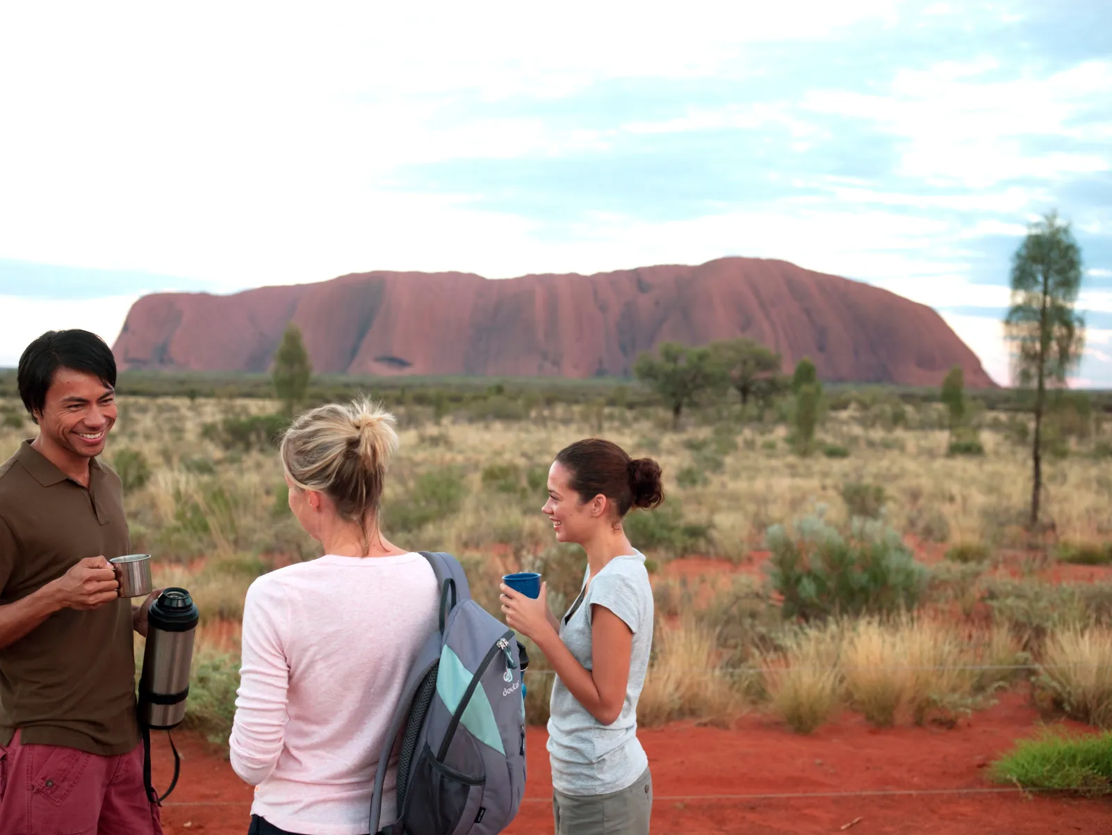 Visitors drinking hot tea from mugs with a thermos at a viewing area in front of Uluru