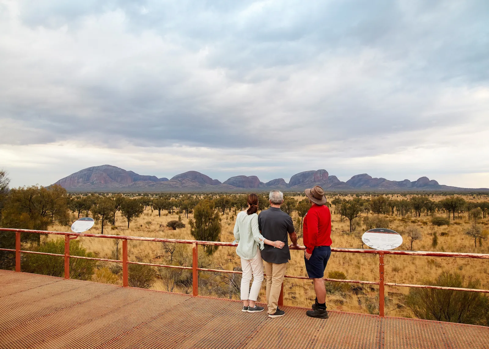 Guide in a red shirt with two guests on a viewing platform facing the line of Kata Tjuta domes