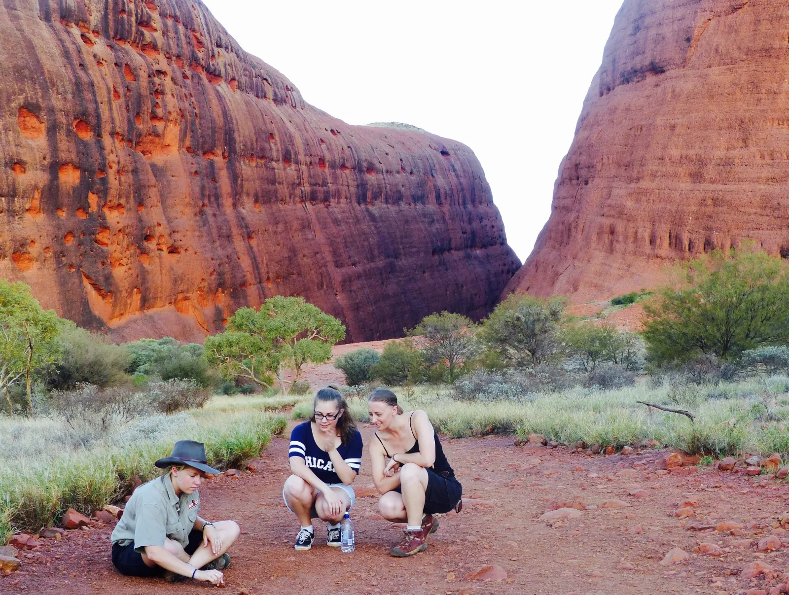Guide crouched on the red track with two guests between the high walls at the mouth of Walpa Gorge