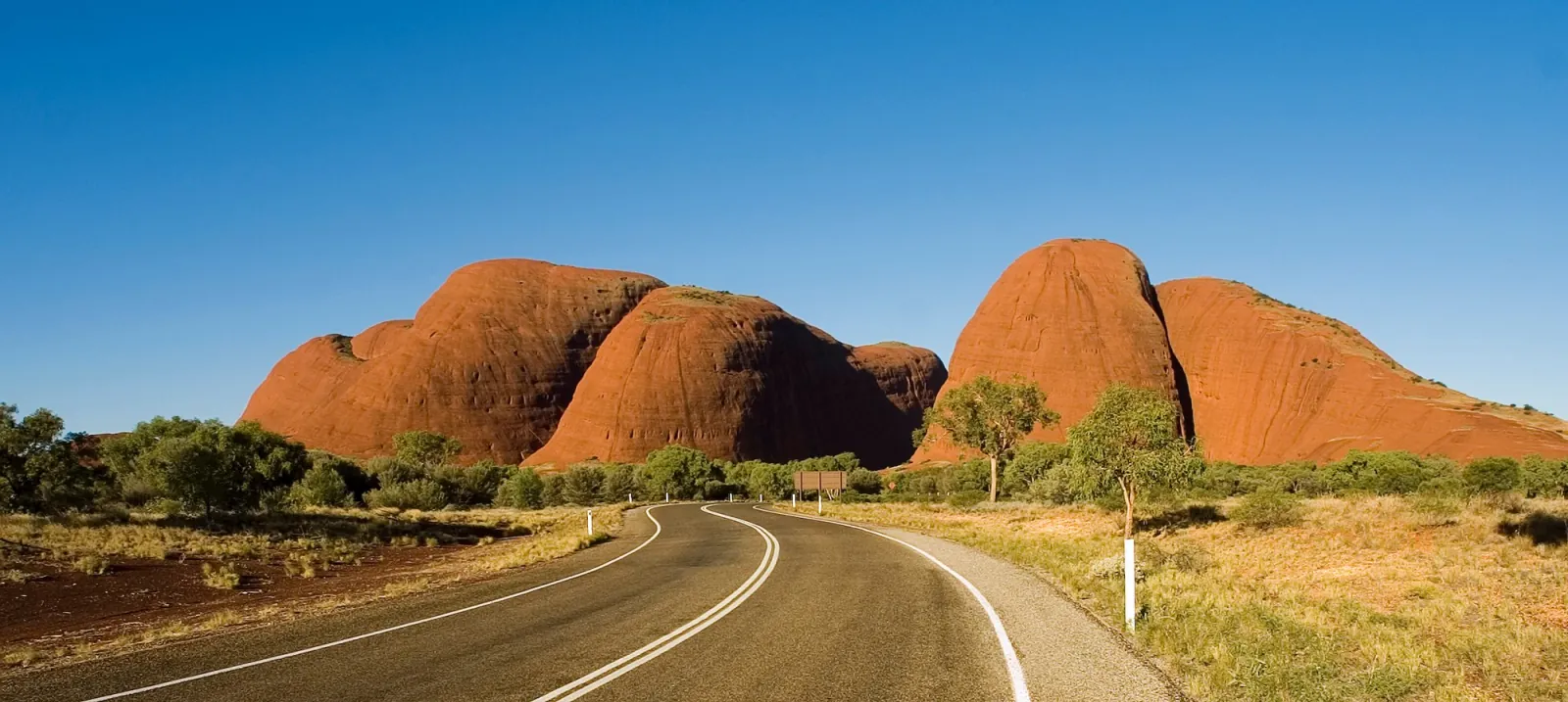 Sealed road curving toward the rounded red domes of Kata Tjuta on a clear morning