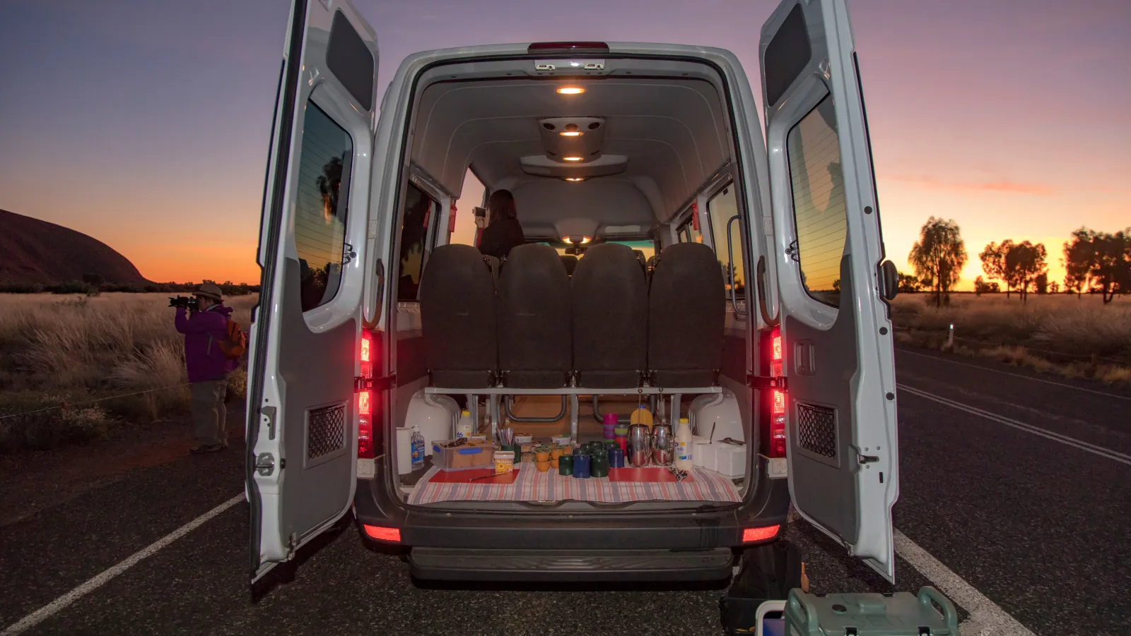 Picnic breakfast with mugs, flasks and cereal laid out in the back of a SEIT van at sunrise
