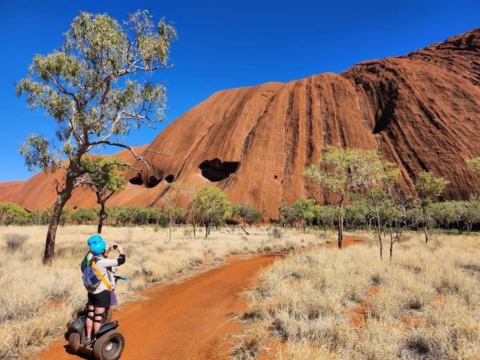 Segway rider stopping on the red base track to photograph caves in Uluru's sunlit face