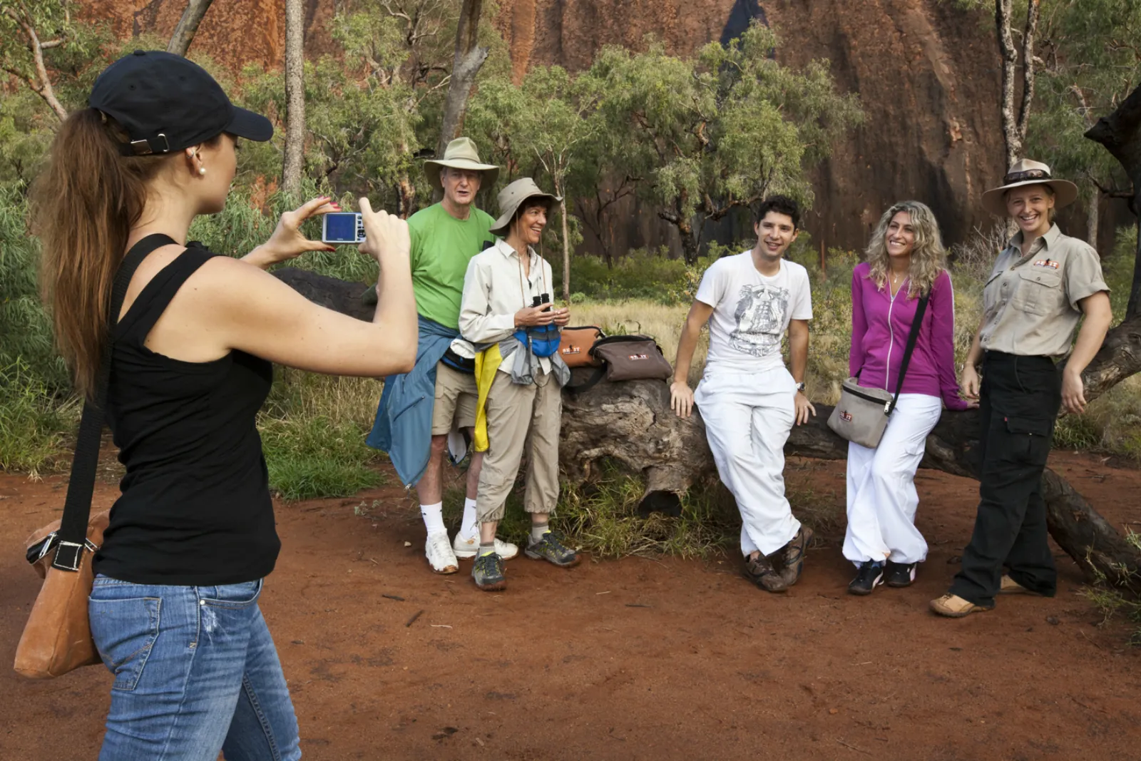 Guest photographing a tour group and guide resting on a log by the base of Uluru