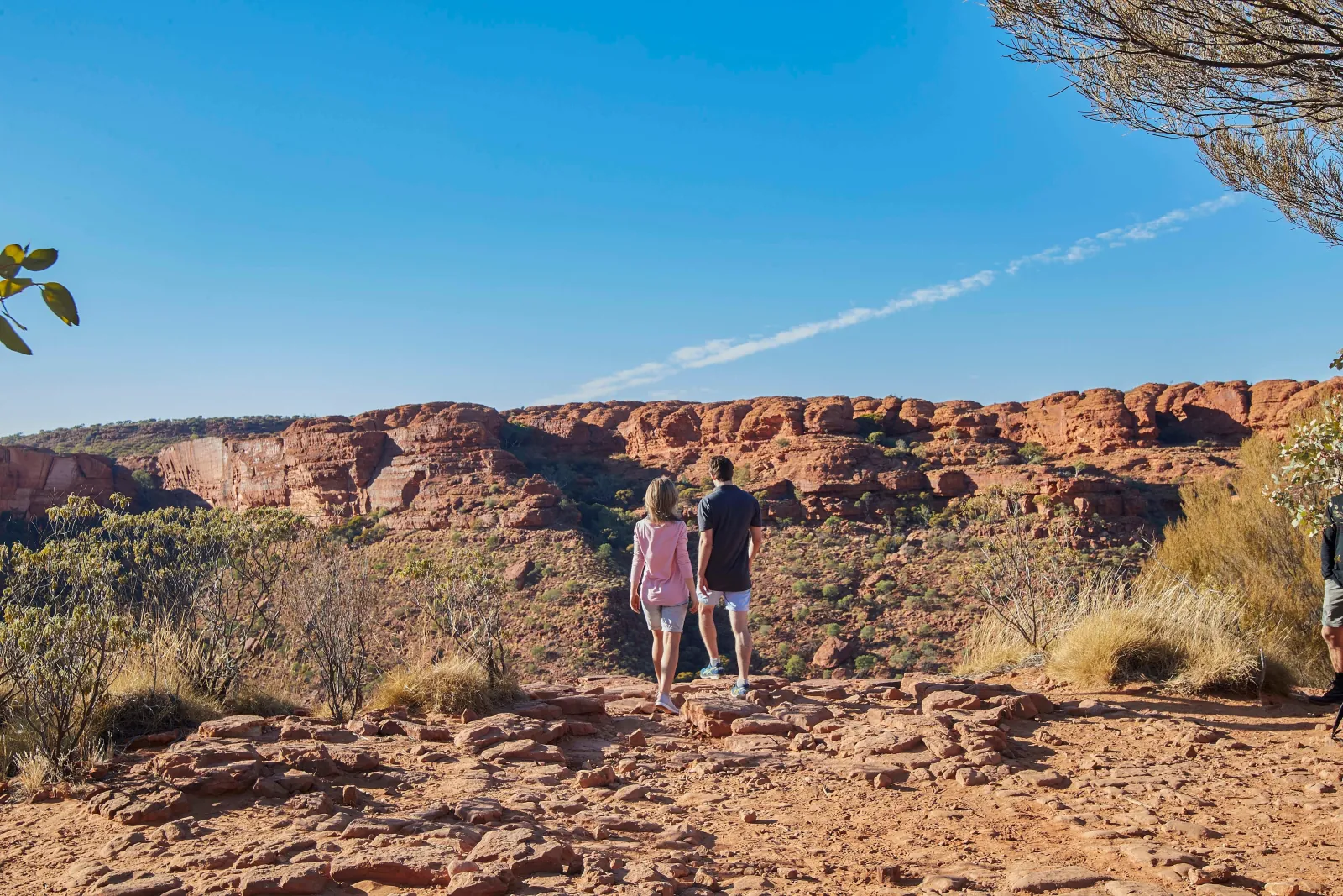 Couple walking across rocky ground toward a line of rounded sandstone domes on the far canyon edge