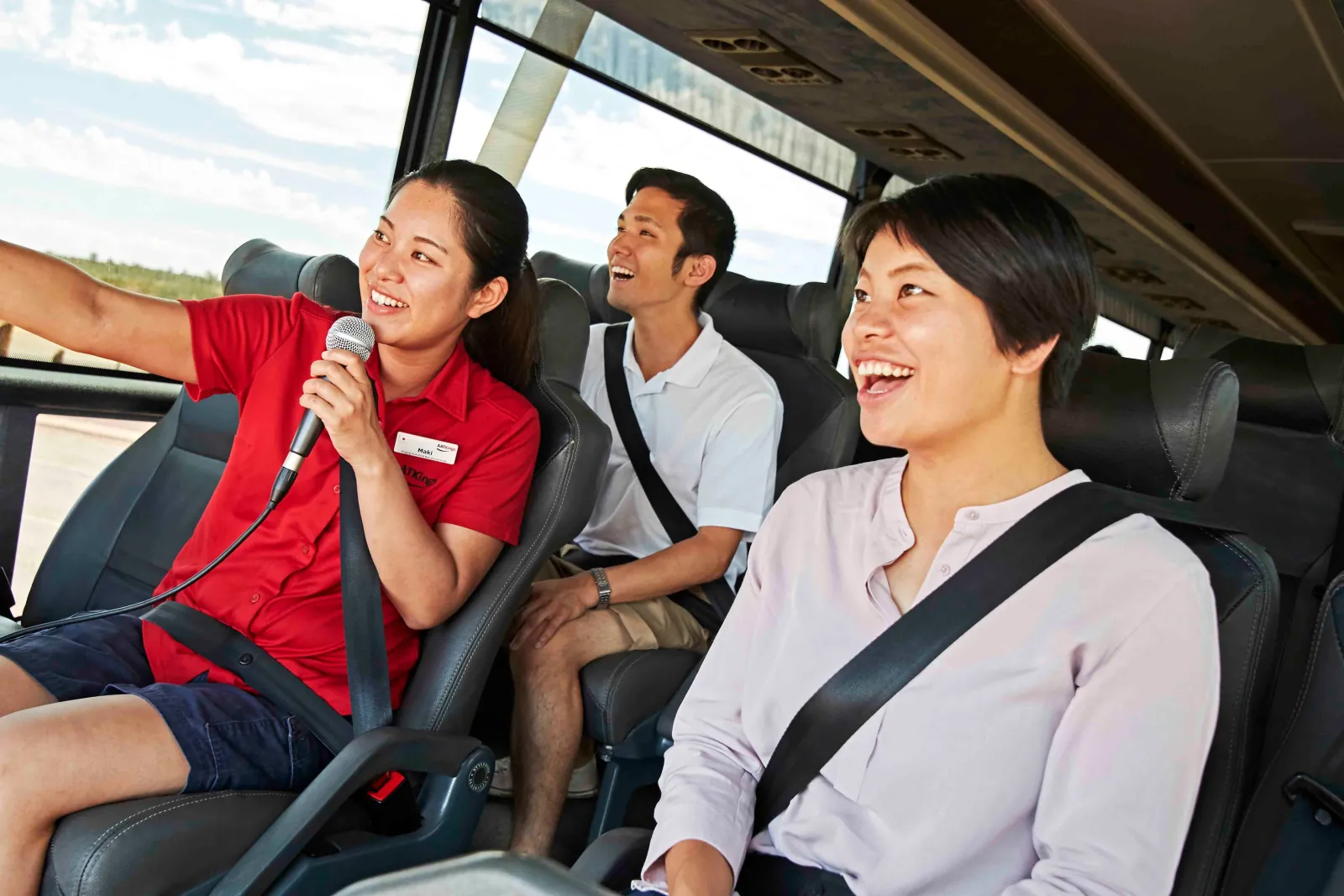 AAT Kings guide in a red shirt giving commentary into a microphone to smiling passengers on board