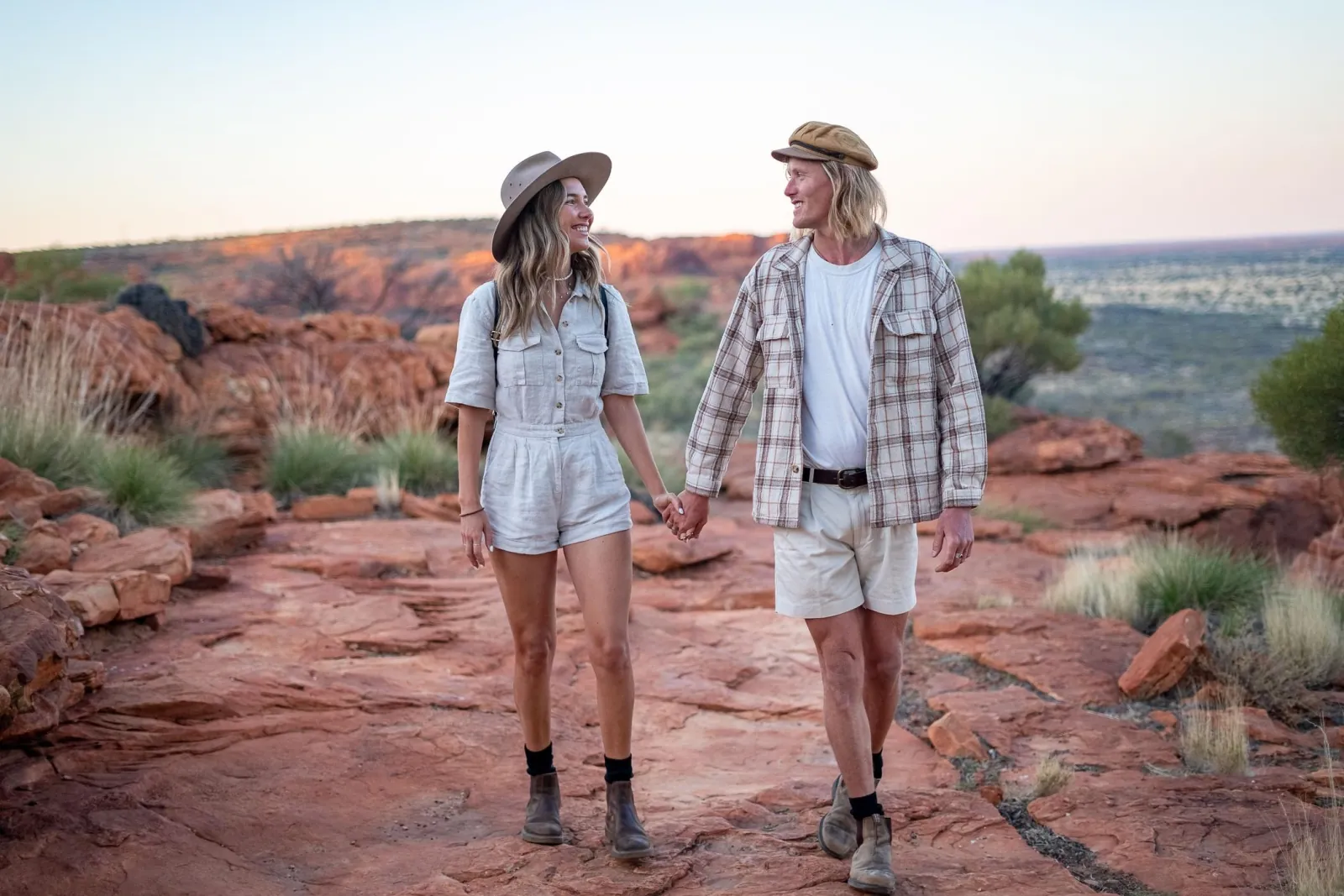 Couple in hiking boots walking hand in hand across red sandstone slabs at golden hour