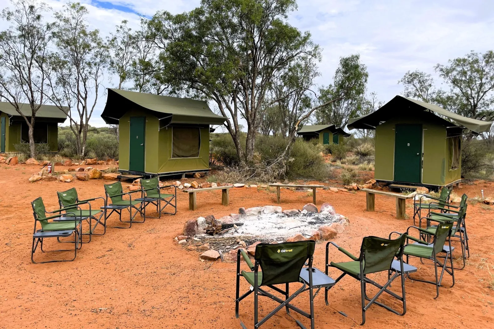 Green canvas eco tents among gum trees, with camp chairs and benches circling a stone fire pit