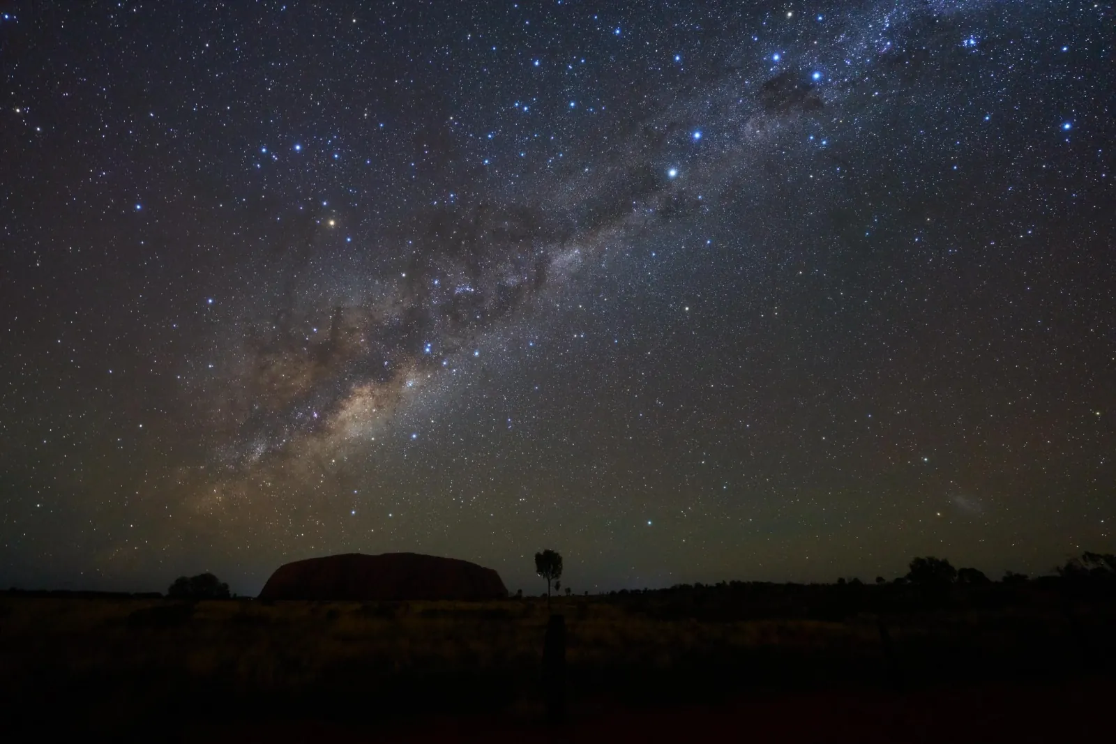 Milky Way arching over the dark silhouette of Uluru on a clear night in the national park