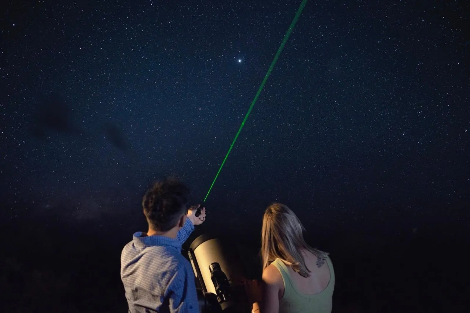 Guide pointing a bright green laser toward a star for a guest beside the telescope