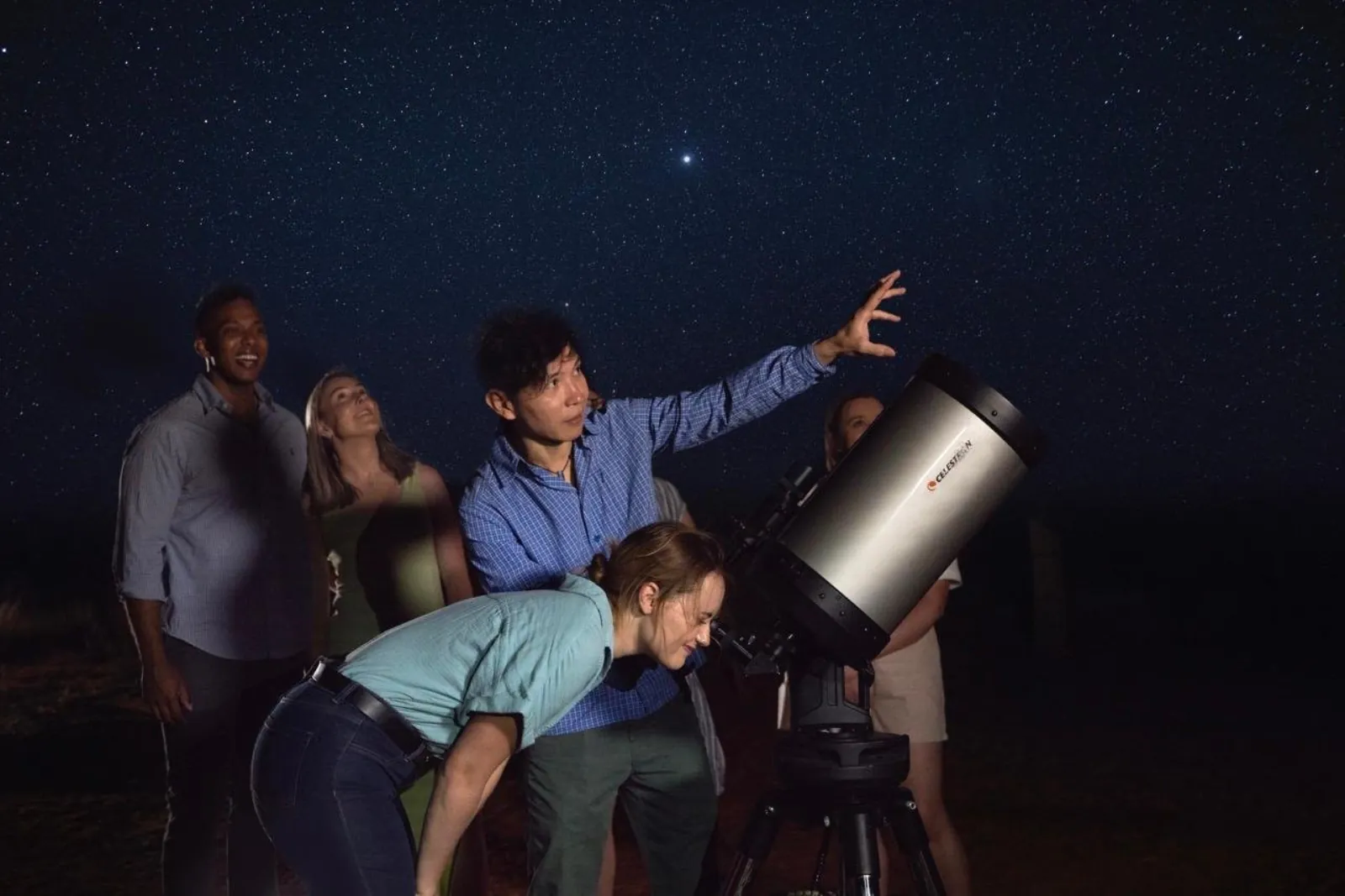 Guide gesturing at the stars as a guest looks through a large Celestron telescope