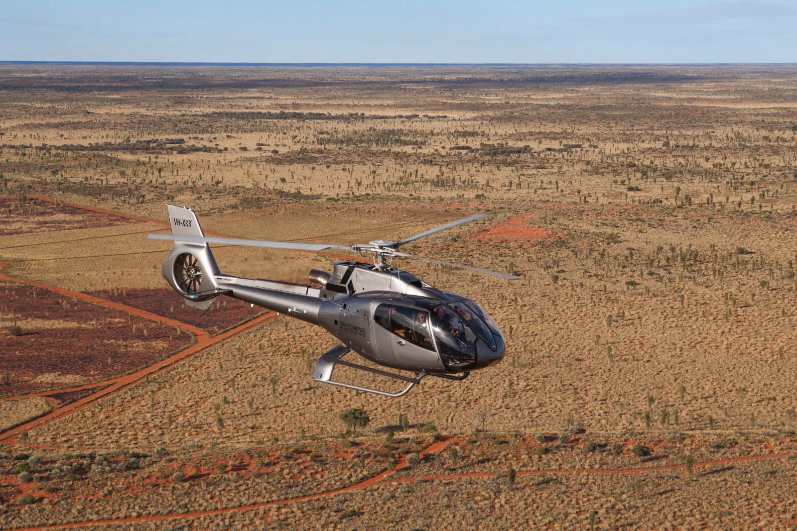 Silver Professional Helicopter Services helicopter flying low over red sand tracks and spinifex