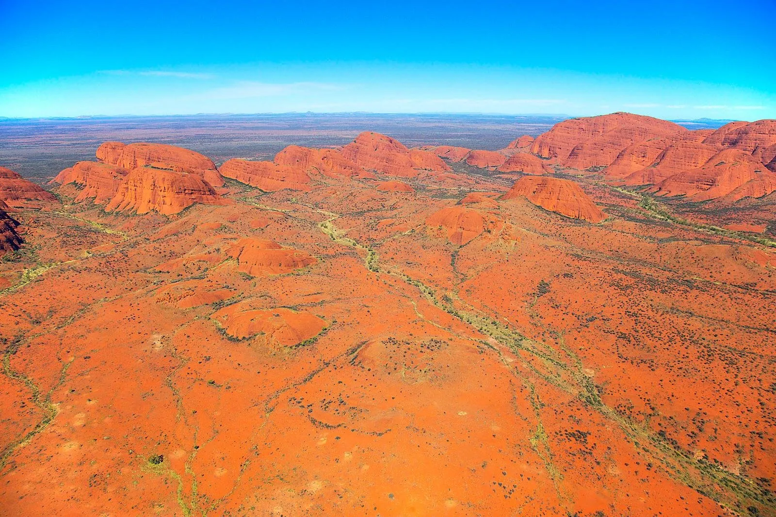 Aerial view of the red domes of Kata Tjuta rising from orange sand plains under a clear blue sky