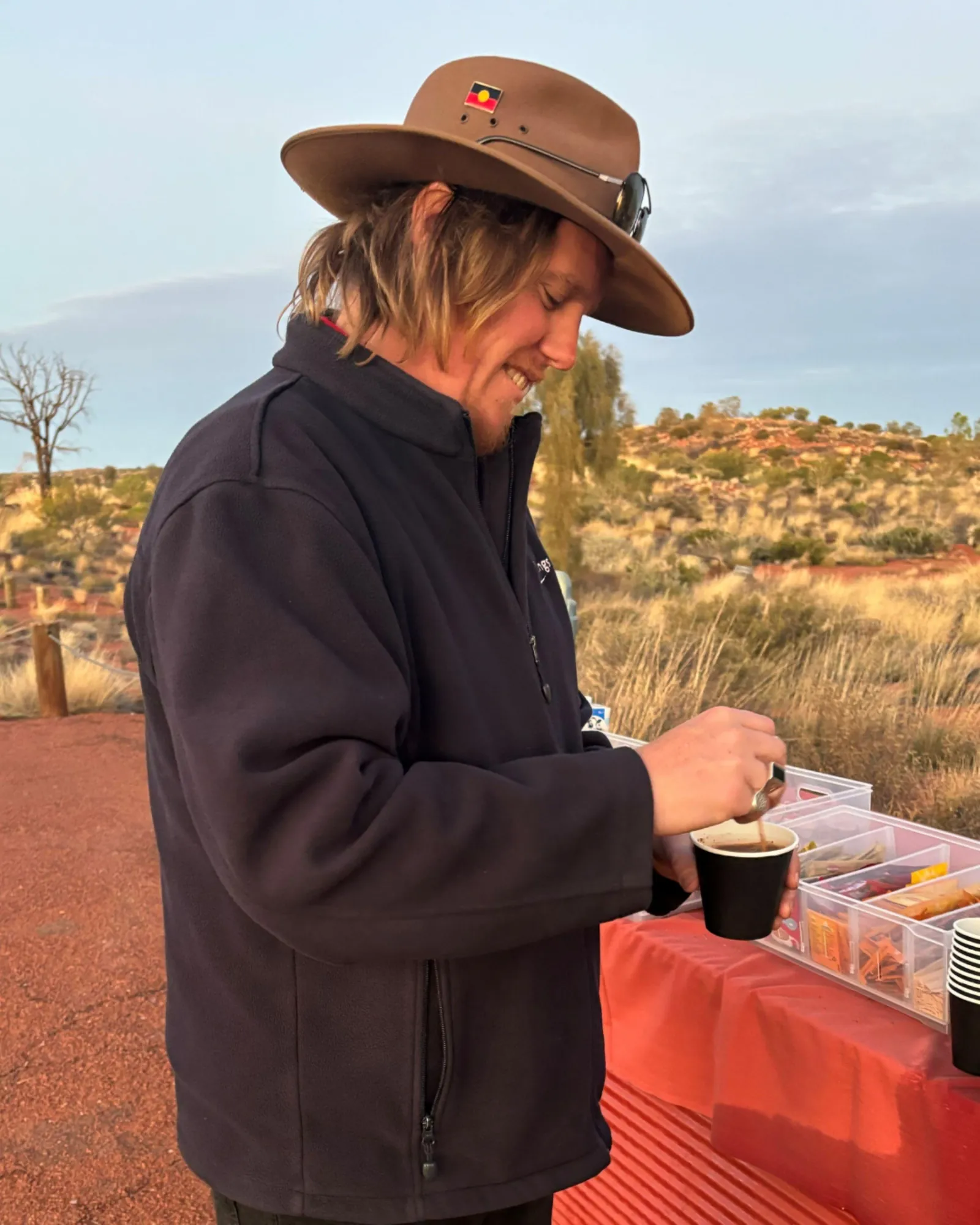 AAT Kings guide stirring a hot drink at the red-covered drinks table on the dune top