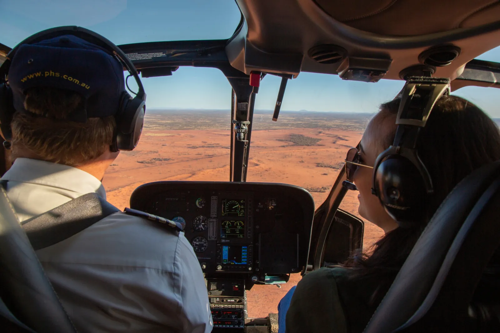 View from the back seat of a pilot in a phs.com.au cap and a passenger looking over red desert