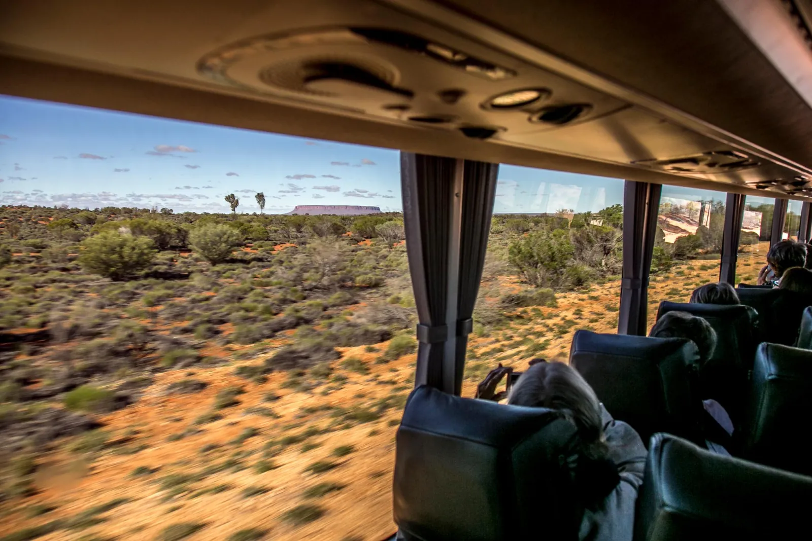 View from a coach window across spinifex and mulga scrub to flat-topped Mount Connor on the horizon