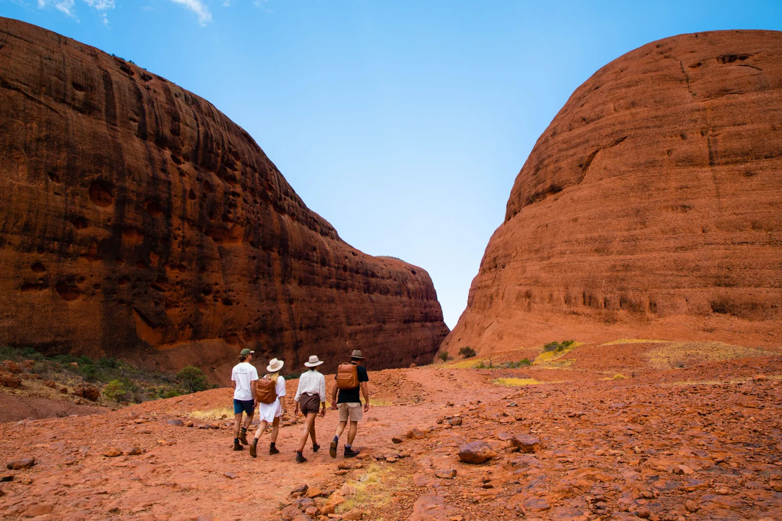 Four walkers with backpacks heading into a gap between two huge rock domes at Kata Tjuta