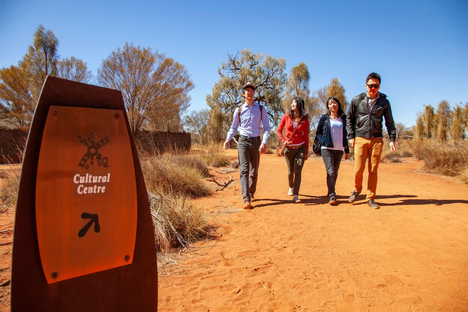 Group of visitors walking a red sand path past a Cultural Centre direction sign