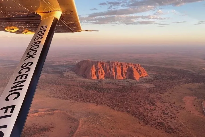 Wing strut marked Ayers Rock Scenic Flights framing Uluru glowing red on the plain below