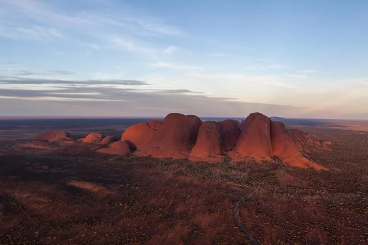 Row of Kata Tjuta domes glowing red at dusk with a winding road on the plain below