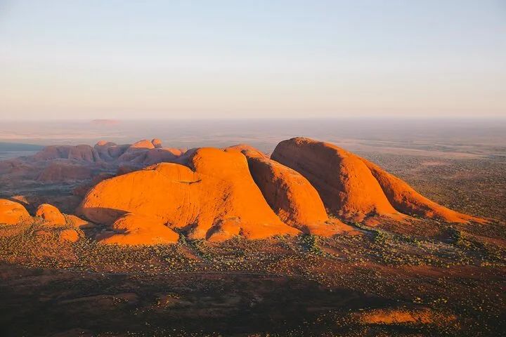 Sunlit orange domes of Kata Tjuta seen from the air with the desert stretching to a hazy horizon
