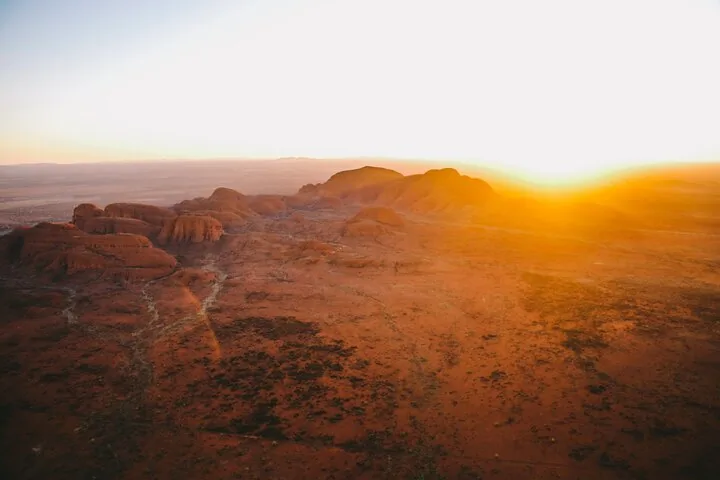 Low sun flaring over Kata Tjuta's domes and creek lines on the red plain, seen from above