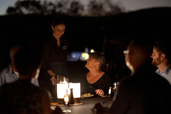 Server smiling at a guest across a candlelit outdoor dinner table after dark