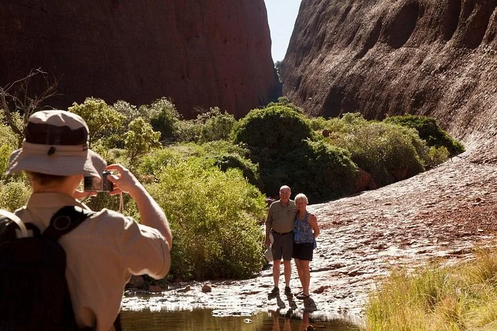 Guest photographing a couple beside a rock pool and green shrubs between Kata Tjuta's walls