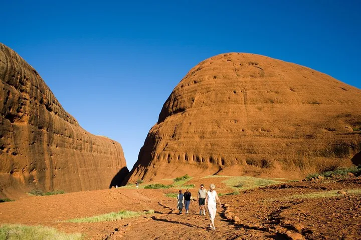 Four walkers on the rocky red track heading between two towering domes of Kata Tjuta