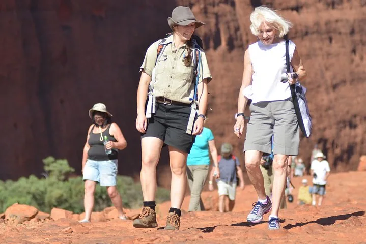 SEIT guide in a bush hat walking with guests over red rock on a Kata Tjuta track