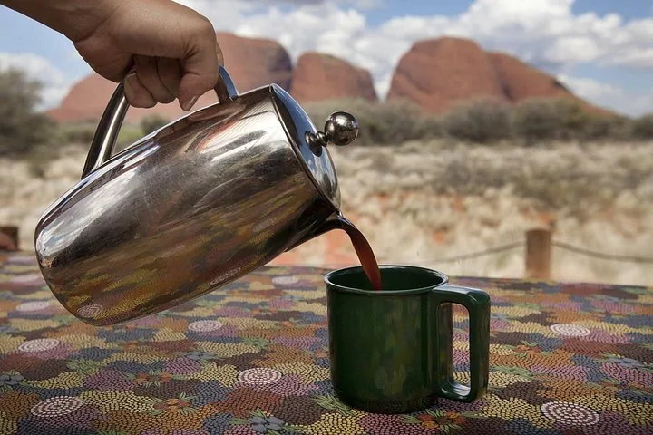 Coffee poured into an enamel mug at the picnic breakfast, with the domes of Kata Tjuta behind