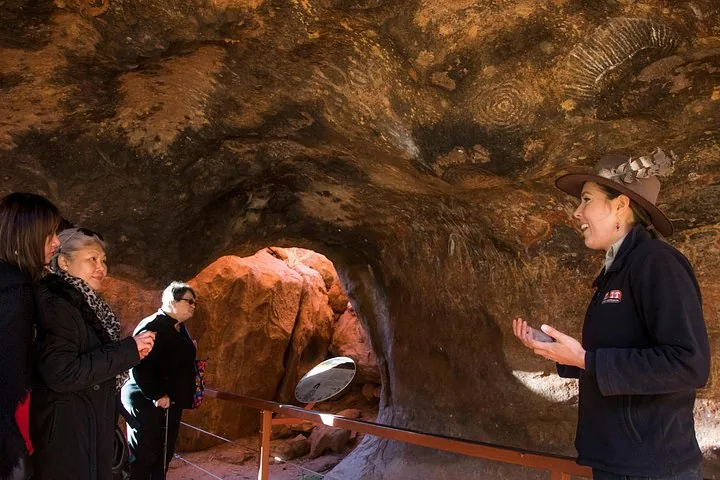 Guide explaining Aboriginal rock art in a cave at the base of Uluru to a small group of guests
