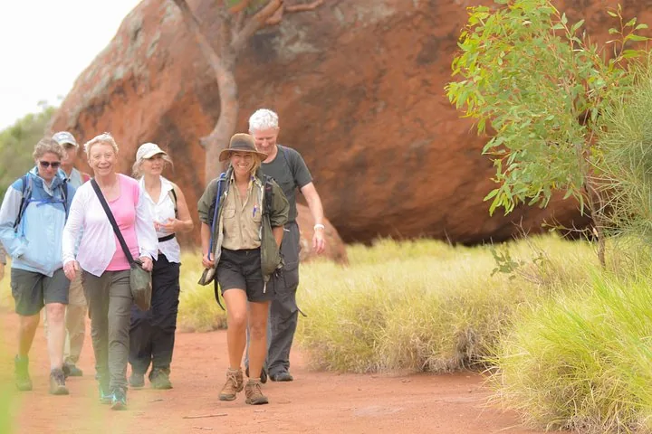 Smiling guide leading a group of walkers past a large red boulder on the Uluru base walk