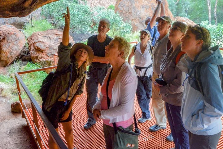 Guide pointing up at the rock overhang to a group standing on a viewing platform at Uluru